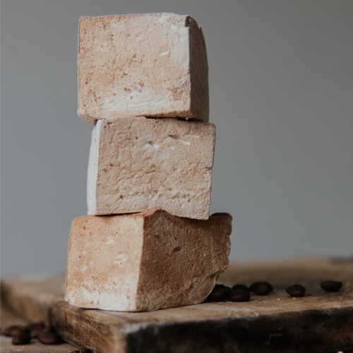 Stack of three beige-colored marshmallows on a wooden surface with coffee beans.