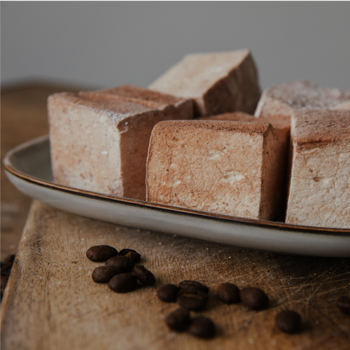 Square marshmallows on a plate with coffee beans on a wooden surface