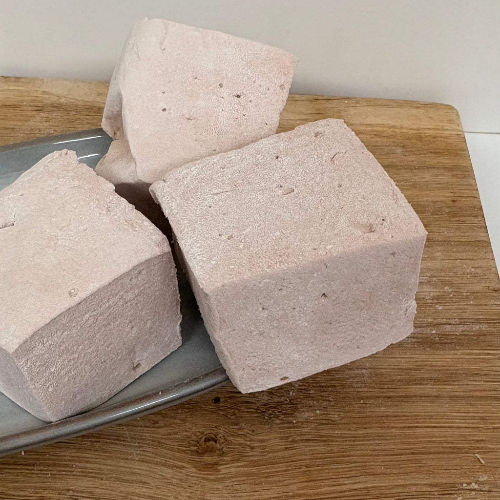 Three beige-colored soft and fluffy marshmallows on a metal tray with a wooden surface underneath