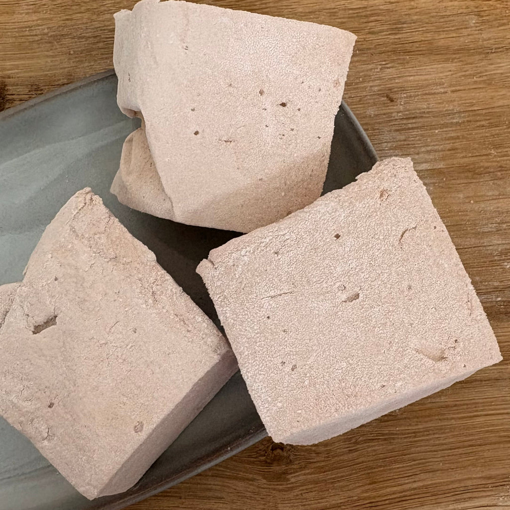 Three square marshmallows on a gray plate with a wooden background